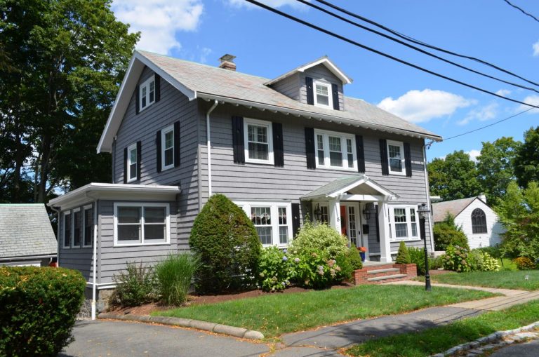 A gray two story home in Bedford, MA with new roofing and gutters installed by O'lyn Roofing.