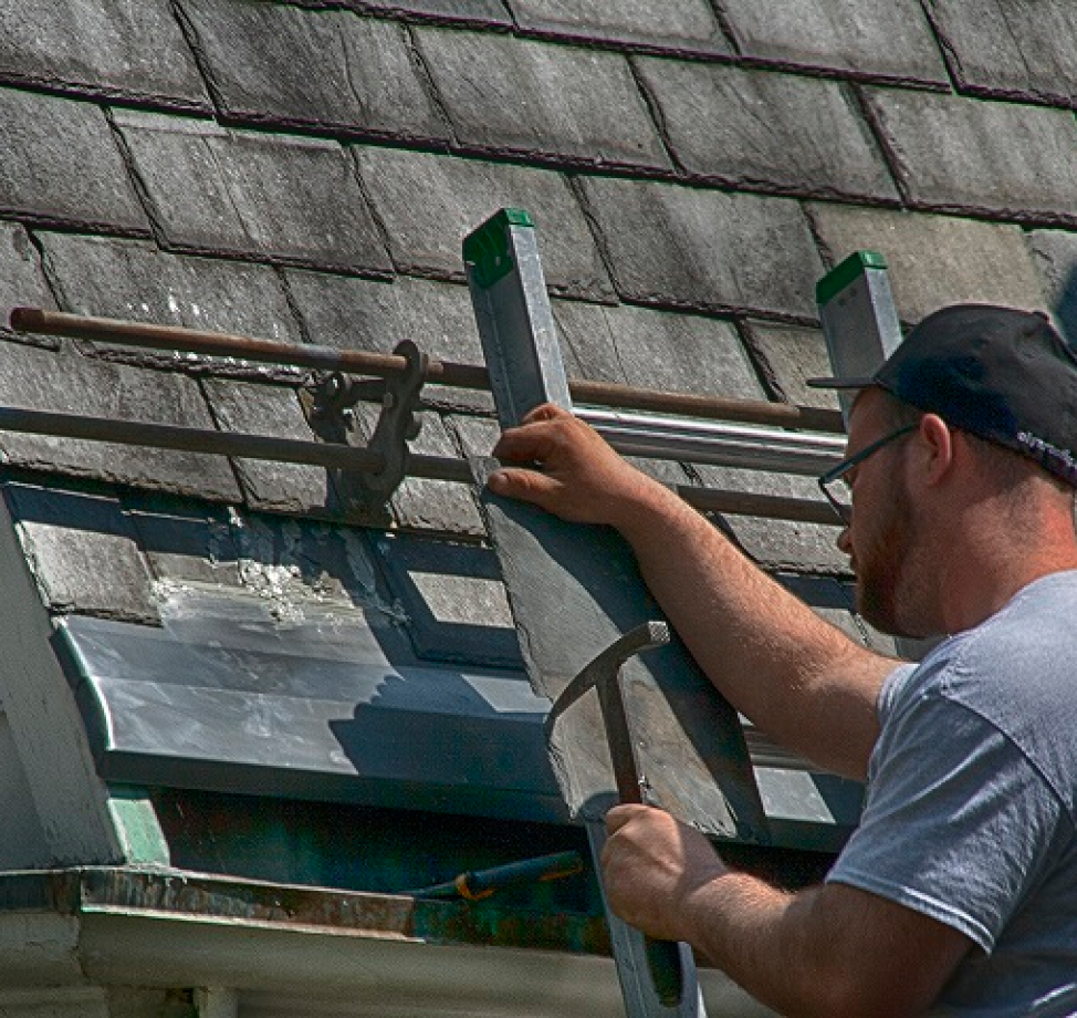 O'LYN employee working on a roof with a hammer in hand.